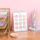 Calendar with floral designs on a desk with stationery items against a pink wall.