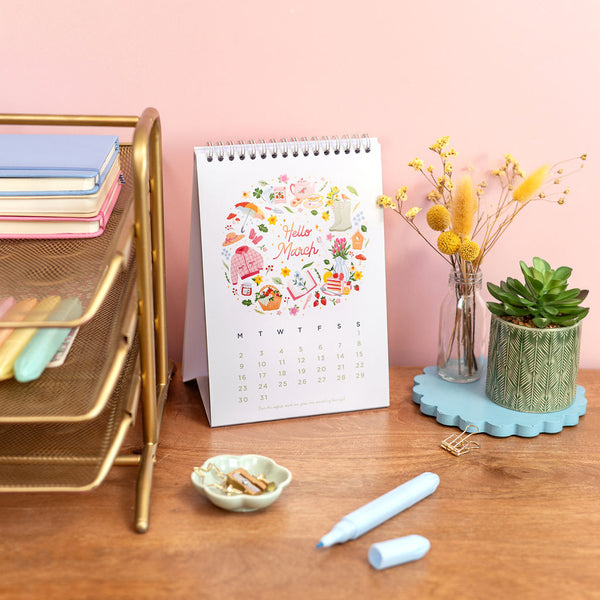 Desk setup with a calendar, stationery, and decorative items on a pink wall background