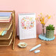 Desk setup with a calendar, stationery, and decorative items on a pink wall background