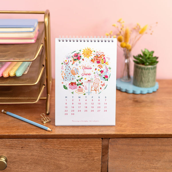Calendar on a desk with stationery items and a pink wall in the background